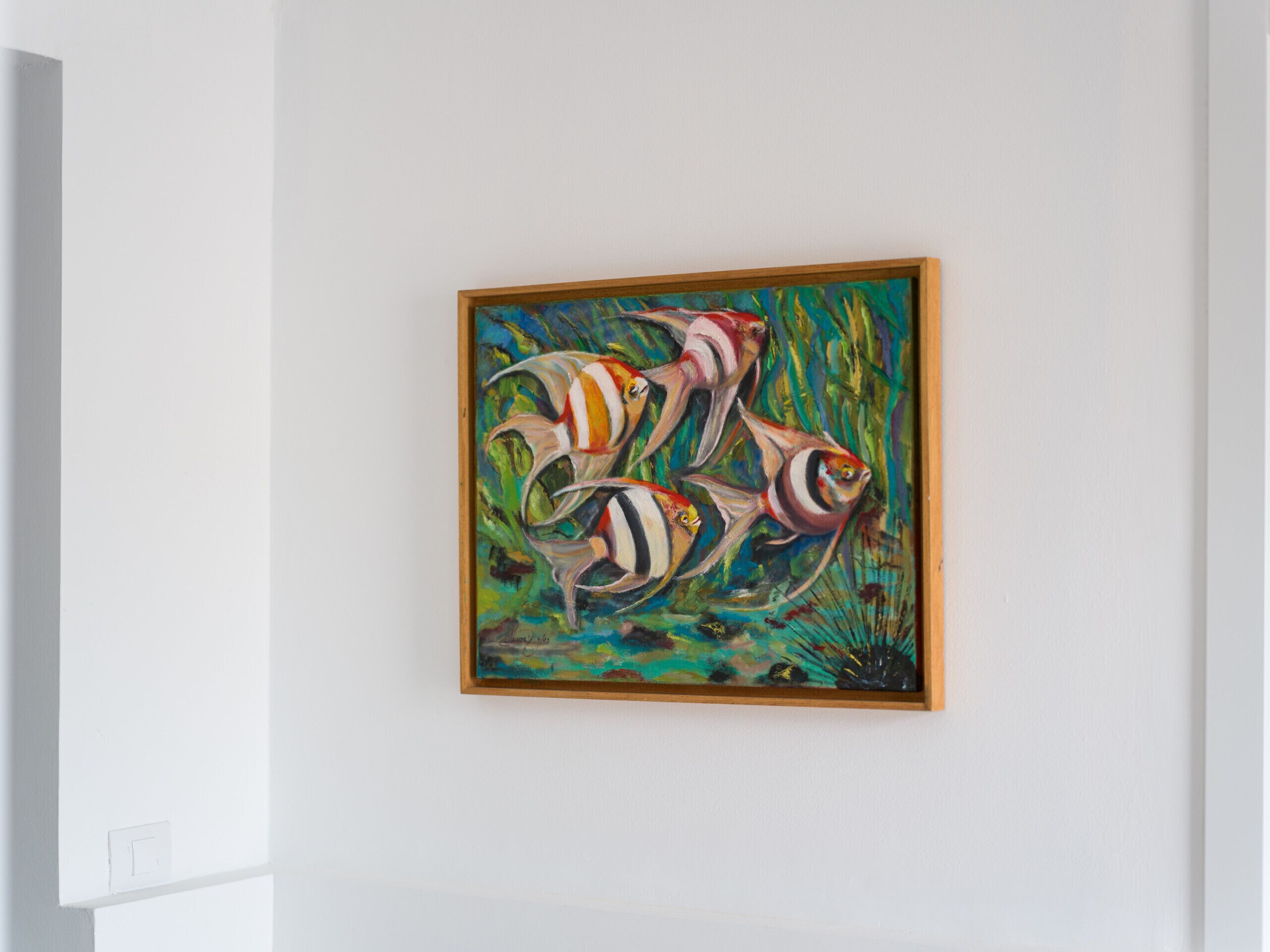 Un tableau encadré représentant des poissons aux couleurs vives, accroché à un mur blanc.