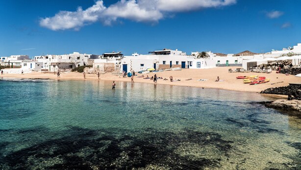 Uma vila costeira com edifícios brancos, águas azul-claras e uma praia de areia.