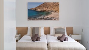 Quarto de hotel com duas camas, uma fotografia grande de praia na parede e cabeceira de madeira.