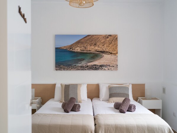 Quarto de hotel com duas camas, uma fotografia grande de praia na parede e cabeceira de madeira.
