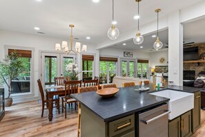 A spacious kitchen with a large island, wooden dining table, and chairs. There are pendant lights, a built-in oven, and a stone fireplace. - MemoRays  Made on Martin, MemoRays Made on Martin- 5BR Lake Front Home- Sleeps 12 (Alexander City)