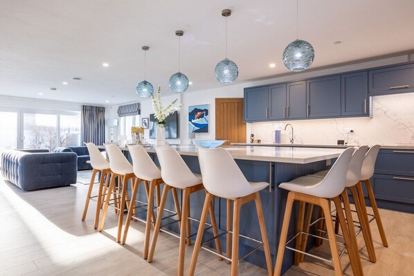 A modern kitchen with a central island, bar stools, and pendant lighting.