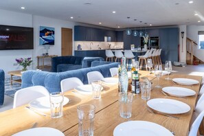 A modern dining area with a wooden table set for a meal, a blue sofa, and a kitchen in the background.