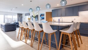 A modern kitchen with a central island, bar stools, and pendant lighting. - The Old Pottery: Spacious 6‑Bed Beach House Sleeping 12 in Rhosneigr | Managed by Anglesey Holiday L (Rhosneigr)