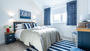 A bedroom with a bed, nightstand, lamp, and a painting on the wall. - The Old Pottery: Spacious 6‑Bed Beach House Sleeping 12 in Rhosneigr | Managed by Anglesey Holiday L (Rhosneigr)