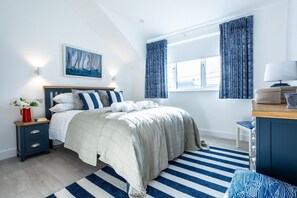 A bedroom with a bed, bedside table, lamp, curtains, and a painting.
