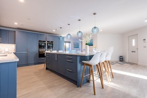 A modern kitchen with dark blue cabinets, stainless steel appliances, and a central island with bar stools.