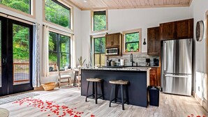 A modern kitchen with large windows, wooden cabinets, and a stainless steel refrigerator. - Cozy cabin in peaceful, serene, wooded setting 20 minutes from area attractions. (Sevierville)