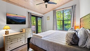 A bedroom with a bed, a dresser, a ceiling fan, and a window with curtains. - Cozy cabin in peaceful, serene, wooded setting 20 minutes from area attractions. (Sevierville)