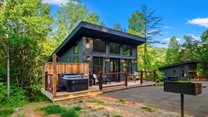 A modern cabin with a deck, hot tub, and outdoor seating area surrounded by trees. - Cozy cabin in peaceful, serene, wooded setting 20 minutes from area attractions. (Sevierville)