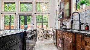 A modern kitchen with large windows, a dining area, and wooden cabinets. - Cozy cabin in peaceful, serene, wooded setting 20 minutes from area attractions. (Sevierville)