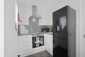 A compact kitchen with white cabinets, a black refrigerator, a microwave, and a stainless steel range hood.