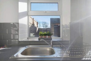 A kitchen with a stainless steel sink, potted plants on the windowsill, and a view of buildings outside. - Relaxing 2BR in Billy Row|WiFi |by Stay With Us (County Durham)