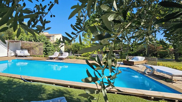 A rectangular swimming pool with a wooden deck, surrounded by lounge chairs and a covered seating area.