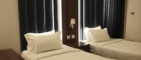 Ein Hotelzimmer mit zwei Einzelbetten, einem Holznachttisch, einer Wandlampe und dunklen Vorhängen.