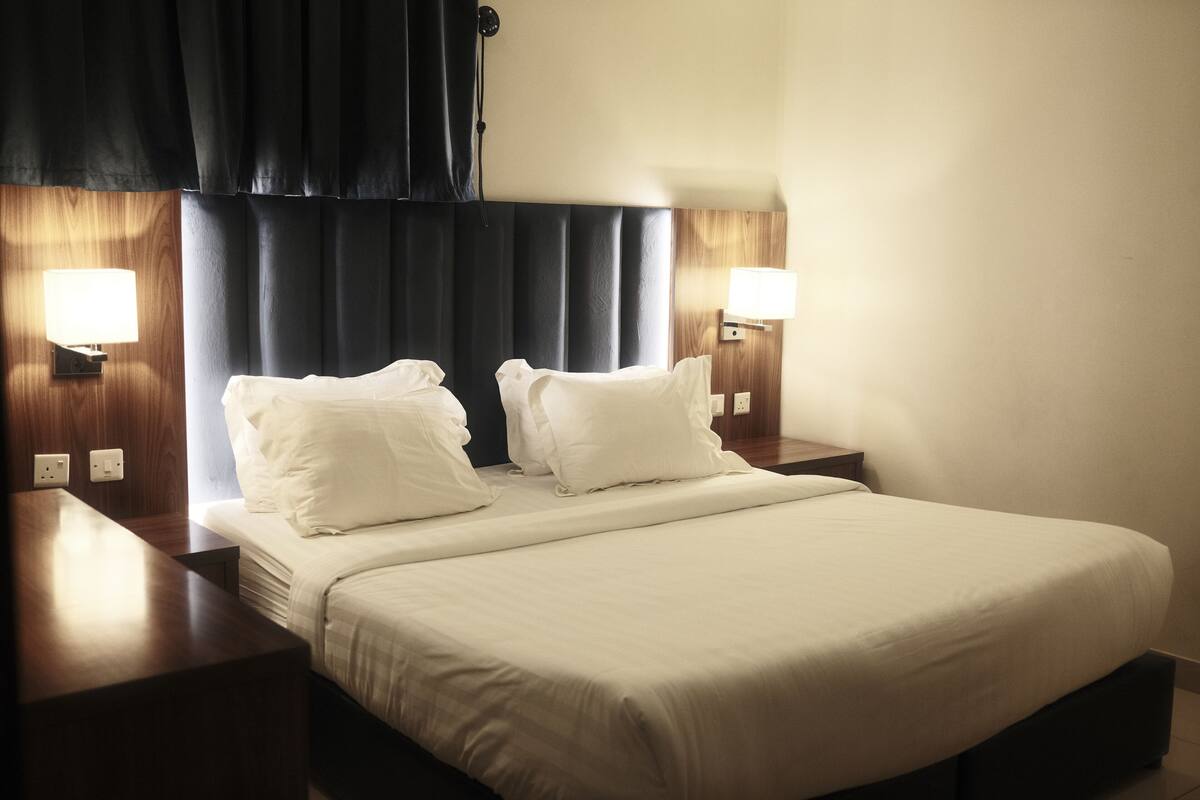A hotel room with a large bed, two bedside tables, and two wall-mounted lamps.
