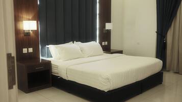 Habitación de hotel moderna con una cama grande, cabecero de madera oscura, mesitas de noche con lámparas y un amplio ventanal con cortinas.