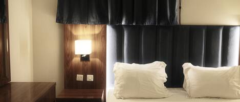 Une chambre d’hôtel avec une table de chevet en bois, une lampe, un lit avec une literie blanche et une tête de lit sombre.