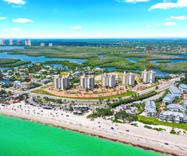 An aerial view of a coastal resort with high-rise buildings, a beach, and surrounding mangrove areas.