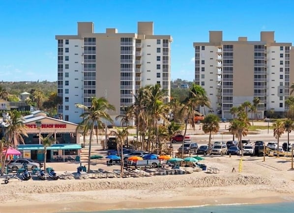 A beachside hotel with multiple high-rise buildings in the background, a beach area with umbrellas and lounge chairs, and a sign for 'Beach House'.