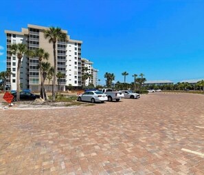 A parking lot with several cars, a building with multiple floors and balconies, and palm trees.