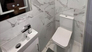 Une salle de bain avec un lavabo blanc, un miroir et des toilettes, le tout mis en valeur par des murs à motifs de marbre.