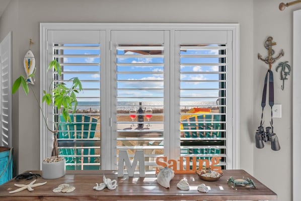 A room with a view of the beach, a wooden table with seashells, a potted plant, and a sign that reads "M Sailing". - Summerwinds Oceanfront Condo | Pools & Beach (Indian Beach)