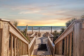 A wooden boardwalk leading to a beach with a sunset in the background. - Summerwinds Oceanfront Condo | Pools & Beach (Indian Beach)