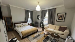 A bedroom with a bed, bedside tables, a sofa, a coffee table, a plant, and a radiator. - Stylish apt in a 1938 building w/parking (London)