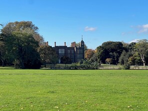 Stately manor house with a traditional tower and multiple chimneys, set amidst a serene and lawn with trees.