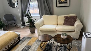 A modern living room with a white sofa, a small round table, a floor lamp, a potted plant, and a radiator. - Stylish apt in a 1938 building w/parking (London)