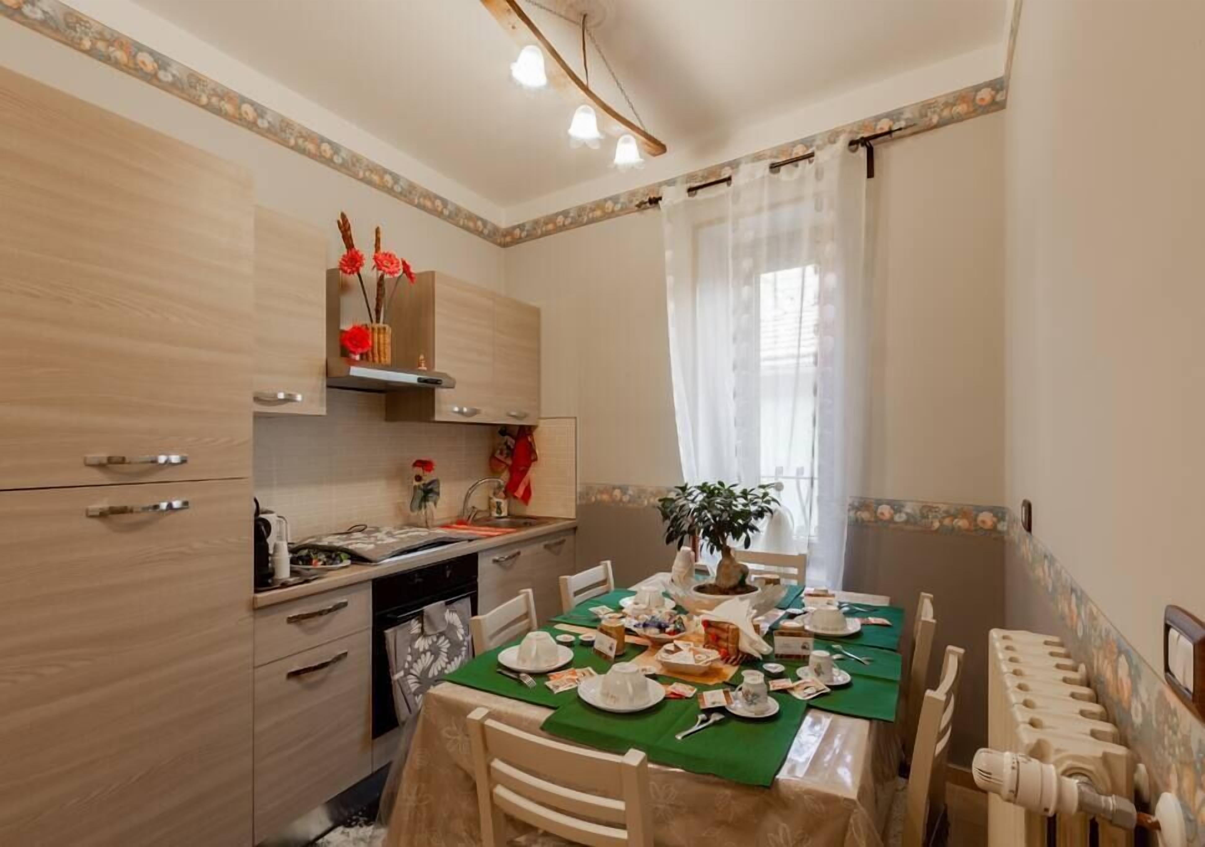 A dining area with a table set for four, a kitchen area with wooden cabinets, and a window with sheer curtains.