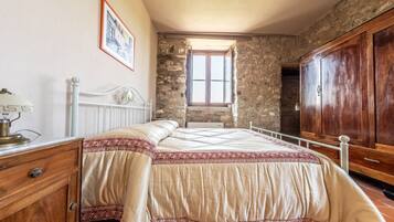 Quarto com cama, guarda-roupa de madeira, paredes de pedra e uma janela.
