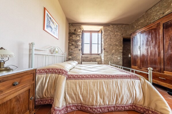 A bedroom with a bed, wooden wardrobe, stone walls, and a window.