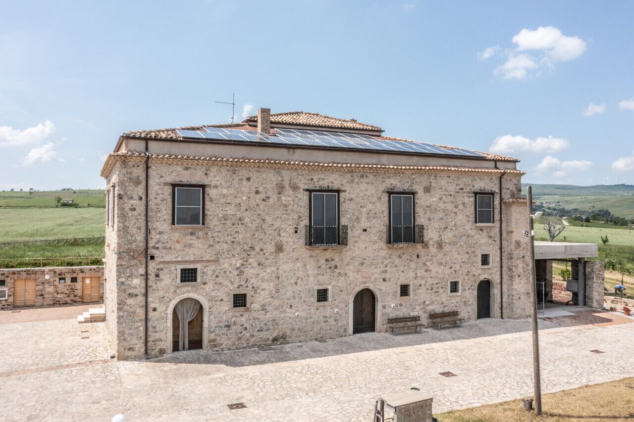 A stone building with a tiled roof, multiple windows, and a paved courtyard.
