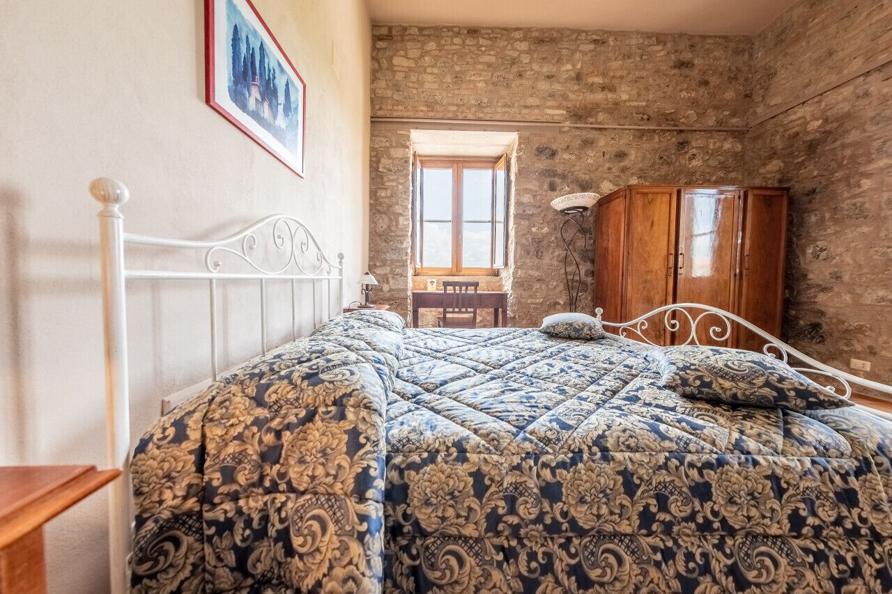 A bedroom with a bed, a wooden wardrobe, a stone wall, and a window.