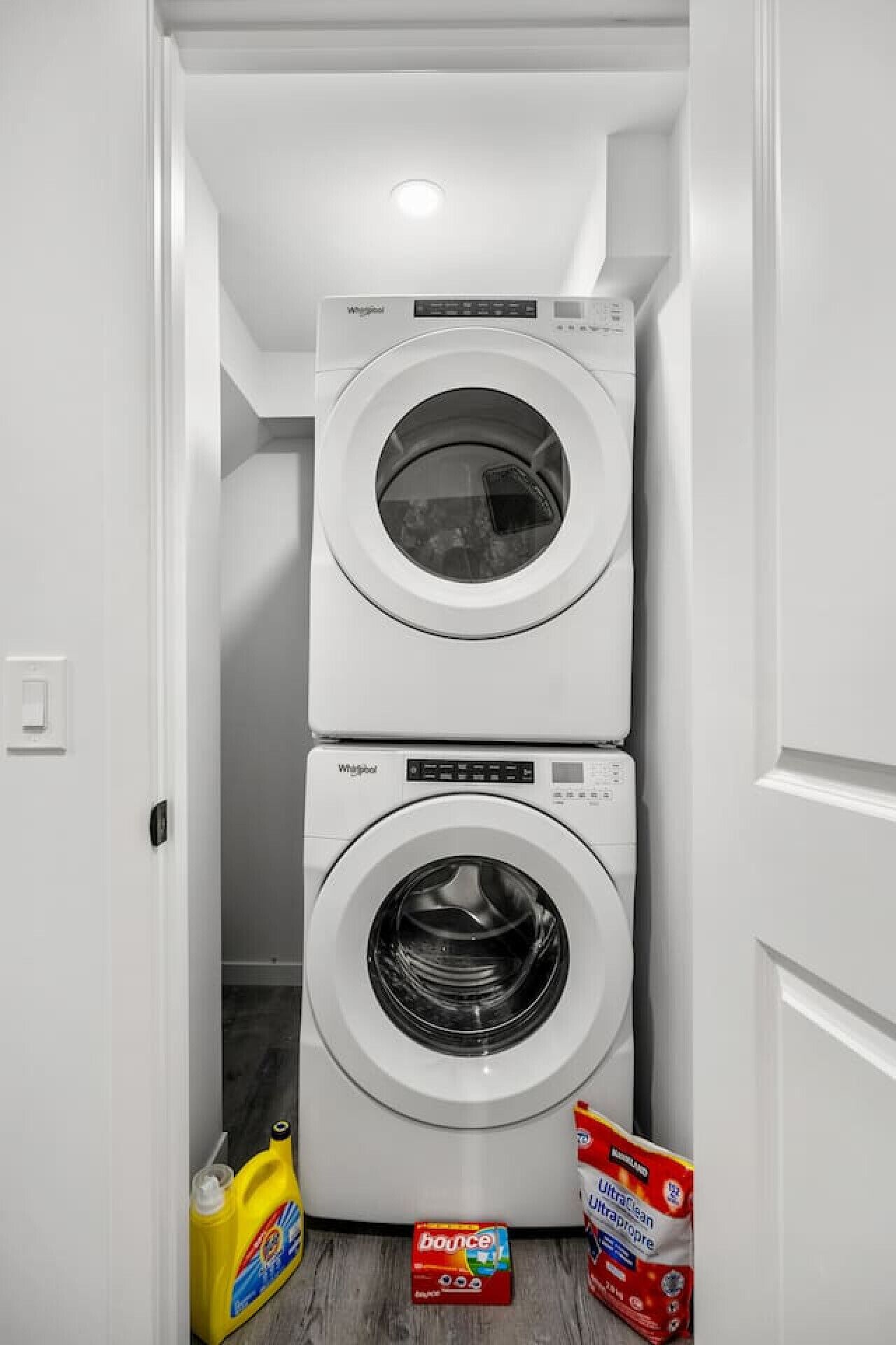 Un lavadero con dos lavadoras Whirlpool de carga frontal apiladas y dos botellas de detergente.