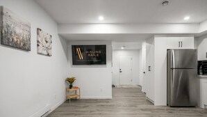 Une cuisine moderne dotée d’un réfrigérateur en acier inoxydable, d’un plancher en bois et d’un couloir menant à une porte.