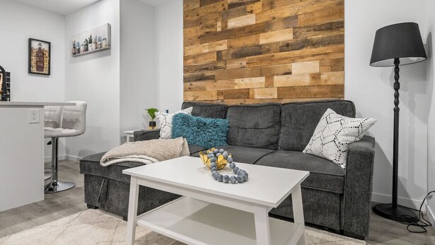 Un salon moderne avec un canapé gris, une table basse blanche et un panneau mural en bois.