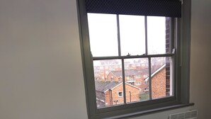 A single bed with white bedding, a dark brown blanket, and two folded towels. A window with a view of residential buildings is above the bed. - Stunning Ensuite Studio at Wolf’s House (London)