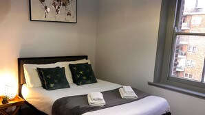A neatly made bed with pillows, a bedside lamp, and a world map artwork on the wall. - Stunning Ensuite Studio at Wolf’s House (London)