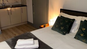 A hotel room with a bed, a small desk with a lamp, a world map on the wall, and a kitchenette with cabinets and a sink. - Stunning Ensuite Studio at Wolf’s House (London)