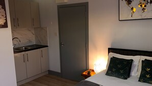 A hotel room with a bed, a small bedside table with a lamp, a world map on the wall, and a kitchenette with cabinets and a sink. - Stunning Ensuite Studio at Wolf’s House (London)