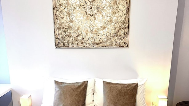 Un letto rifatto con due cuscini, un'opera d'arte appesa al muro e comodini con lampade.
