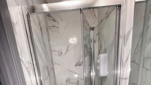 Una cabina doccia in vetro con soffione a mano e dispenser per sapone a portata di mano.