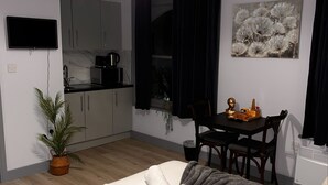 Una camera da letto moderna con un letto, comodini, un piccolo tavolo da pranzo e una zona cucina sullo sfondo.