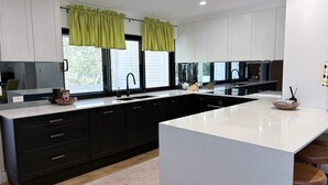 A modern kitchen with black cabinets, a white countertop, and green curtains.