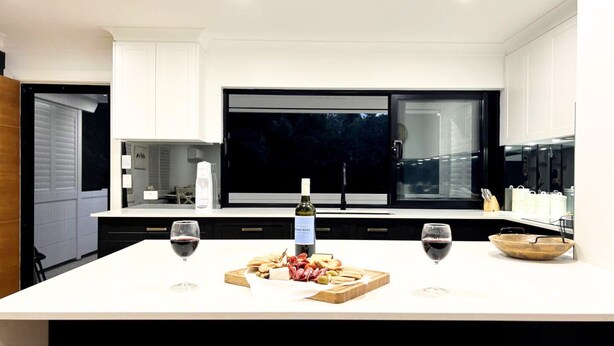 A modern kitchen with a large island, wine glasses, a bottle of wine, and a charcuterie board.