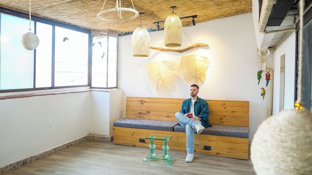 Una stanza con una panca in legno, lampade appese in vimini e un piccolo tavolo verde.