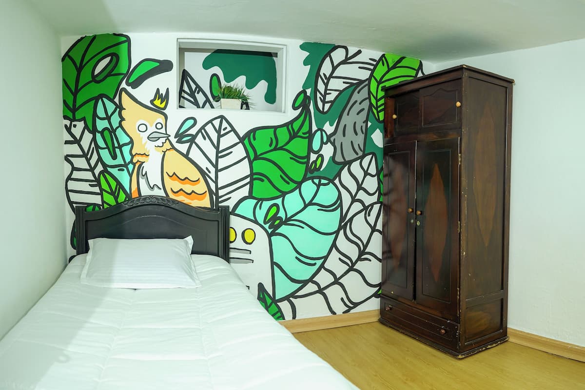 A bedroom with a bed, a wooden wardrobe, and a wall mural.